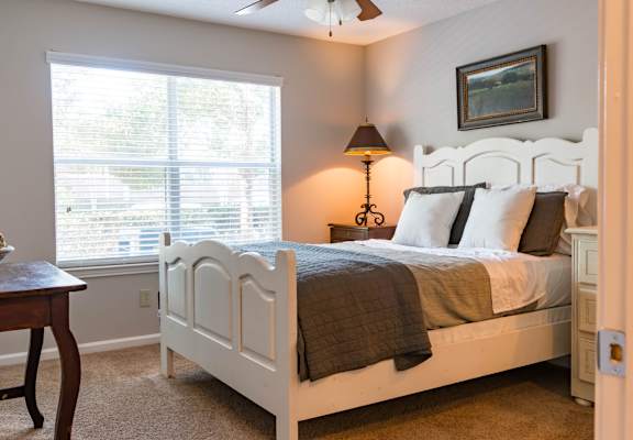 A bedroom with a white bed and a window with blinds.