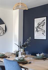a dining room with a wooden table and blue chairs and a blue wall with artwork