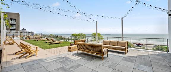A patio with wooden furniture and string lights overlooking the ocean.