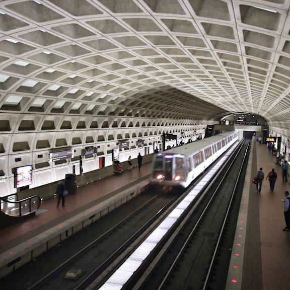 A subway train is pulling into a station with people waiting on the platform.