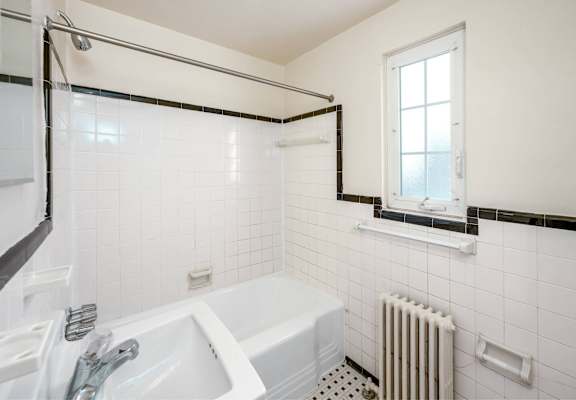 A white bathroom with a tub, sink, and window.