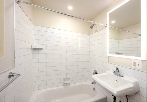 A white bathroom with a sink, mirror, and bathtub.