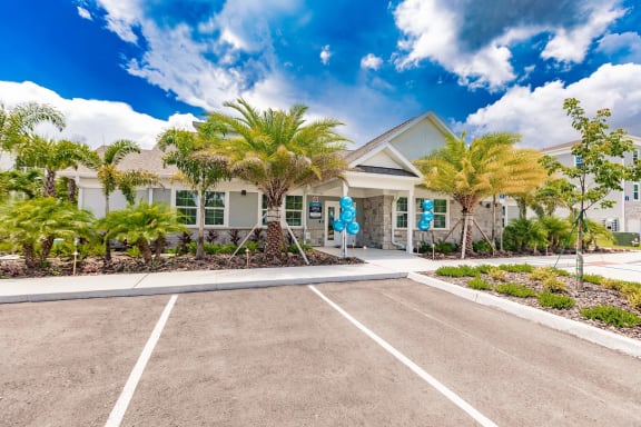 swiftwater apartments clubhouse exterior with a parking lot and palm trees in front of it