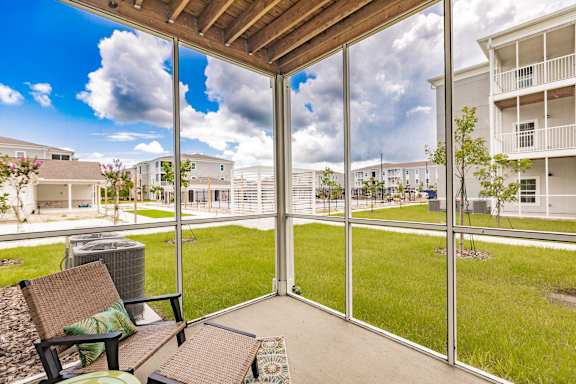 A patio with a bench and a table is shown with a view of a grassy area and buildings.