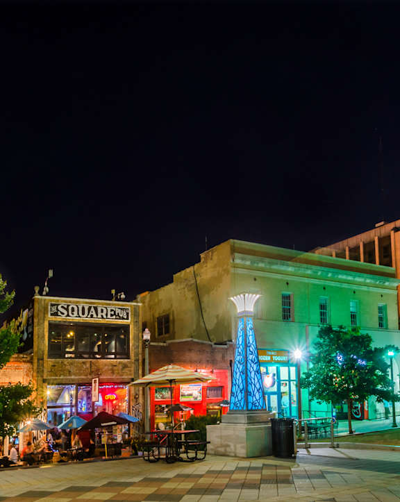 A city square at night with a lit up monument in the foreground.
