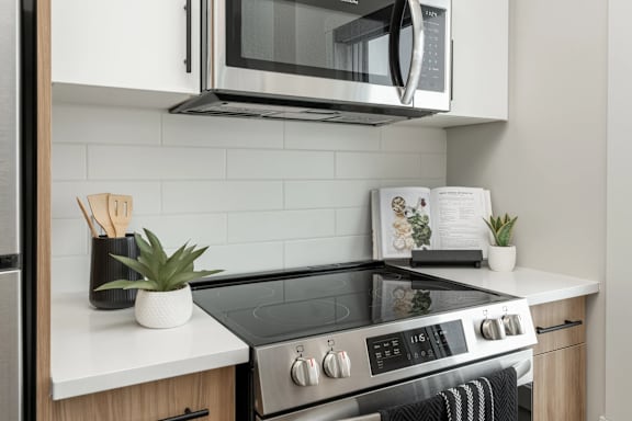 A modern kitchen with a stove top oven and a microwave above it.at Latitude 49 Townhomes, Manitoba