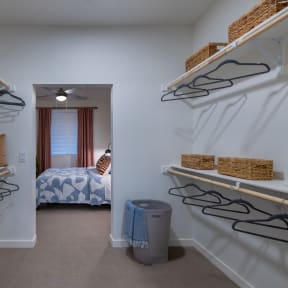 a walk in closet with shelves and racks and a bedroom with a bed