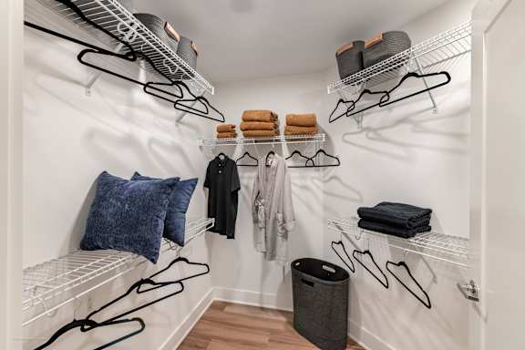 a walk in closet with two wire racks and a white robe and a red jacket