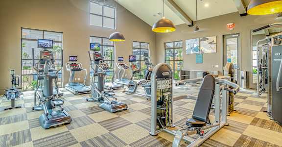 A gym with a variety of equipment including treadmills, stationary bikes, and weight machines at Stone Loch Apartments, Tomball, TX