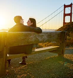 a couple sitting on a bench in front of the golden gate bridge