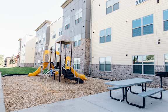 A playground with a yellow slide and a picnic table in front of a building.
