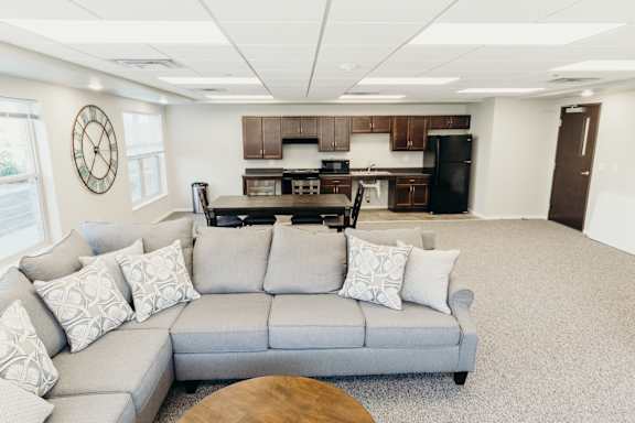 A living room with a grey couch and a kitchen in the background.