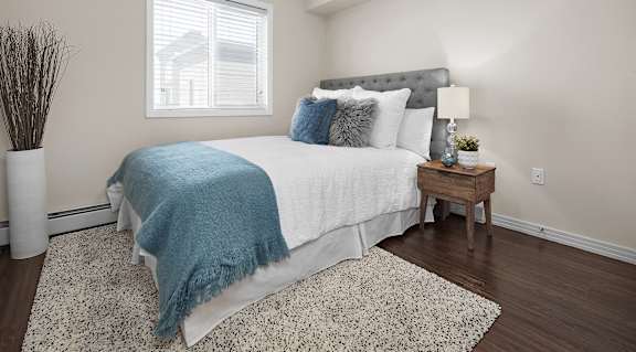 A bedroom with a bed covered in a blue blanket and a small table with a lamp on it.
