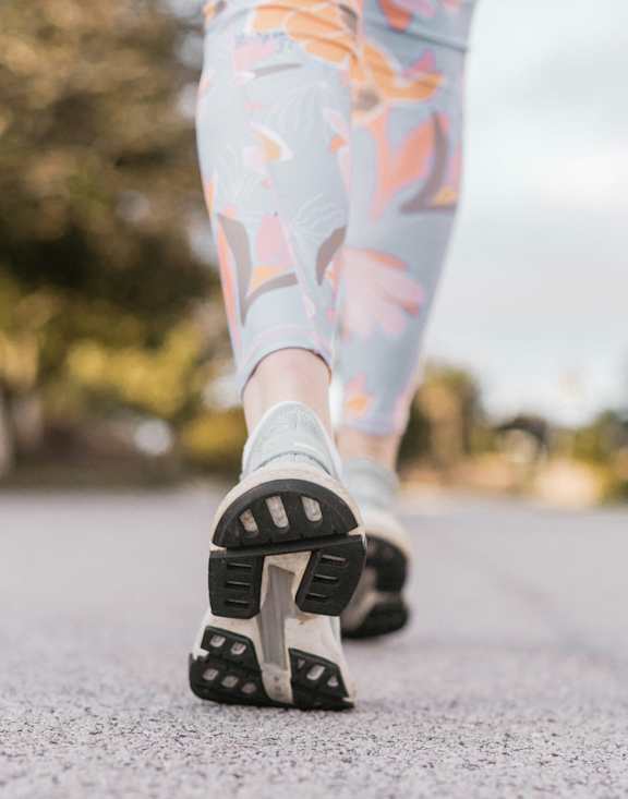 A person is walking on a grey surface wearing floral patterned pants and black shoes.
