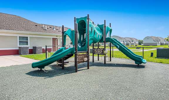 A playground with a green slide and a brown sign.