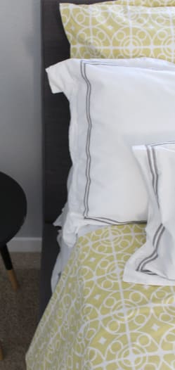 A bed with white pillows and a yellow patterned skirt.