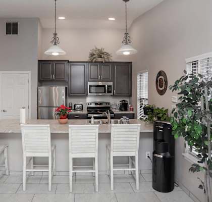 A kitchen with white chairs and a black trash can.