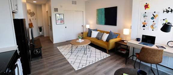 a living room with a yellow couch and a desk with a laptop