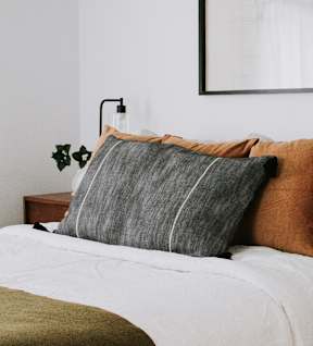 A bed with a white comforter and a wooden nightstand with a plant on it.