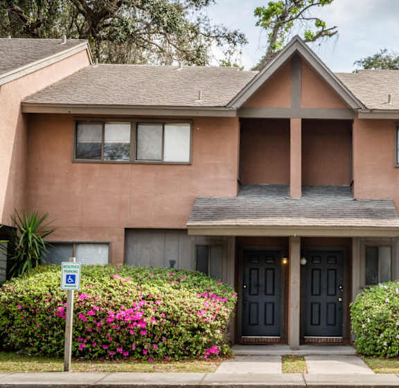 the front of a brown house with bushes and a sidewalk