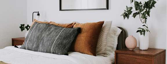 A bed with a white comforter and a wooden nightstand with a plant on it.