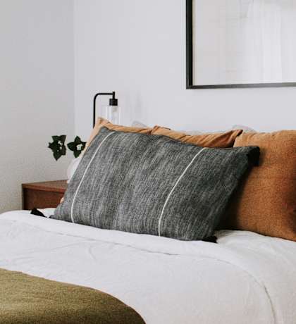A bed with a white comforter and a wooden nightstand with a plant on it.