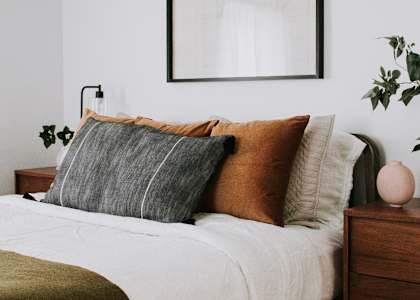 A bed with a white comforter and a wooden nightstand with a plant on it.