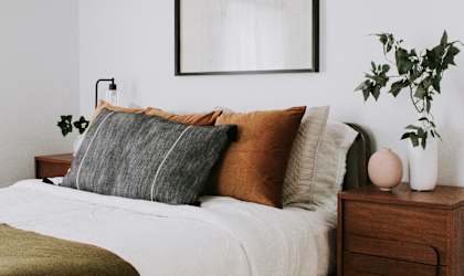 A bed with a white comforter and a wooden nightstand with a plant on it.