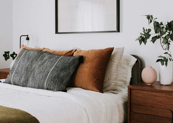 A bed with a white comforter and a wooden nightstand with a plant on it.