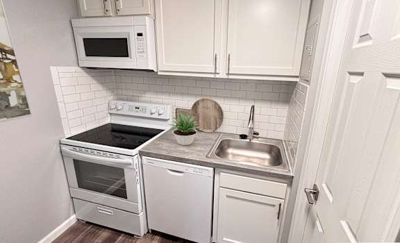 A white kitchen with a stove, oven, dishwasher, and sink.