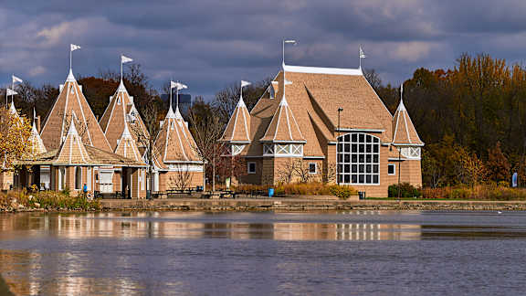 A building with a brown roof and white trim is reflected in the water in front of it.