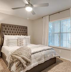 A bedroom with a bed, a fan, and a dresser.