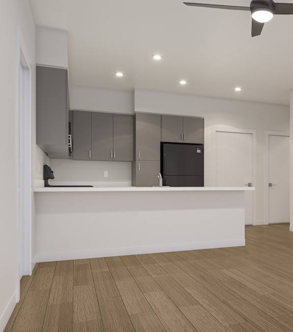A room with a ceiling fan and a kitchen area with a fridge and microwave.