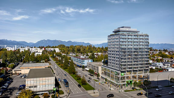 A modern building with a glass facade stands tall in the center of a bustling city intersection.