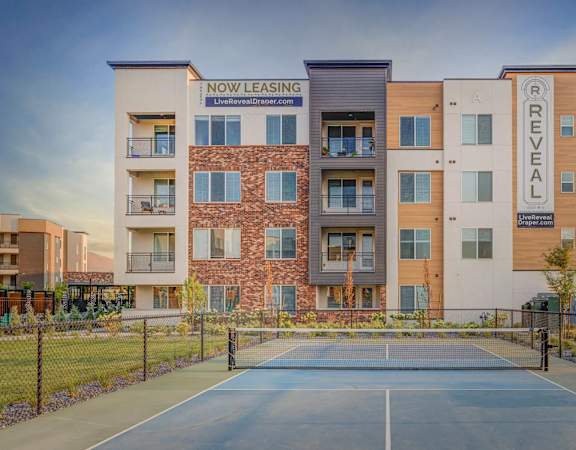 A tennis court is in front of a multi-story apartment building.