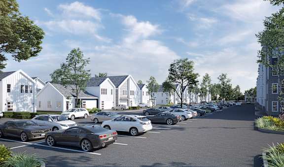 A parking lot with cars and a row of houses in the background.