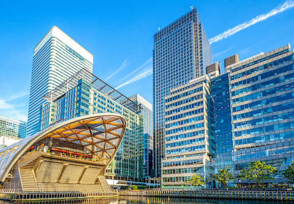 A modern building with a curved glass facade sits next to a body of water.