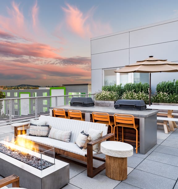 A patio with a fire pit and seating area overlooking a cityscape at dusk.
