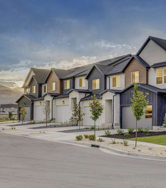 An exterior view of townhomes with front lawns, attached garages, and mountains in the background at Mt. Rainier townhouses for rent in Herriman, Utah.