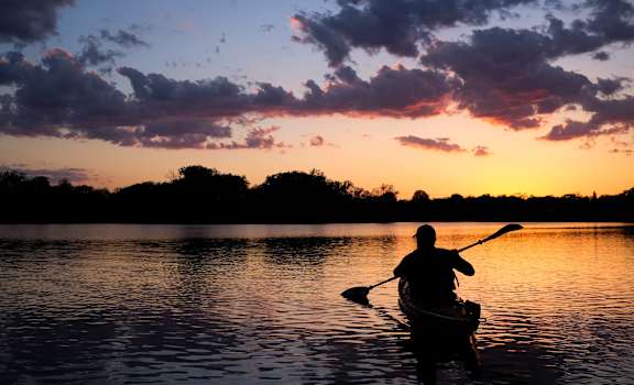 a man in a kayak on a lake at sunset