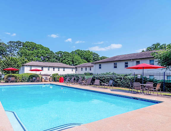 a swimming pool with chairs and umbrellas in front of a resort style pool at Avondale Station Apartments in Decatur, GA