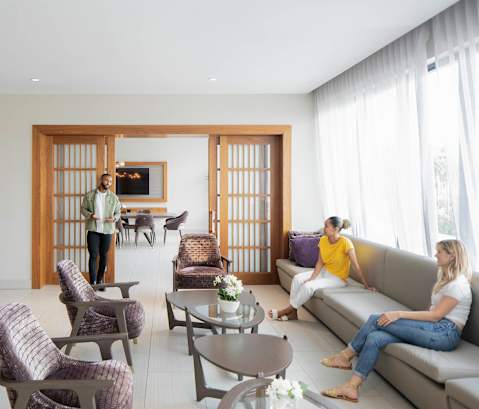 A man in a striped shirt is standing in a living room with two women sitting on a couch. at Palma, Doral, FL, 33166