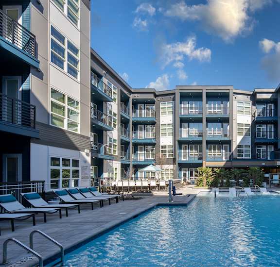 A swimming pool in front of a building with lounge chairs around it.