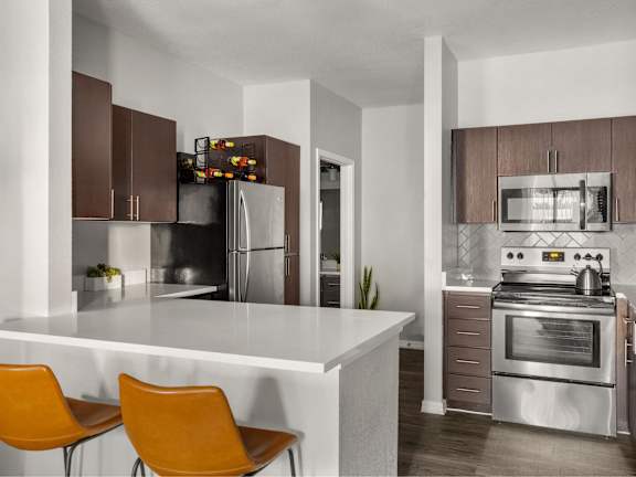 A modern kitchen with a white island and orange chairs.