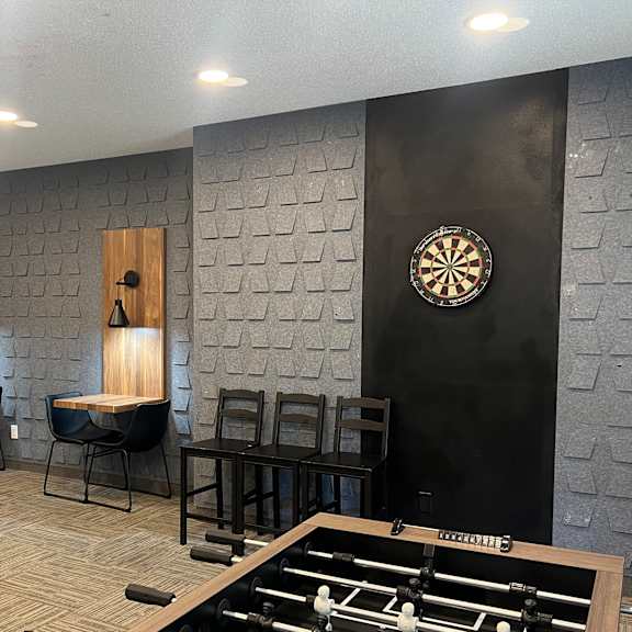 A foosball table is in the middle of a room with a dart board on the wall.