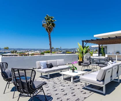 A patio with a white couch, chairs, and a table with a view of the city.