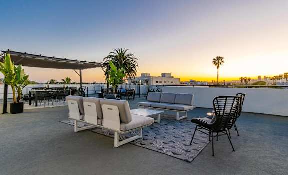 A patio with a white couch, a black chair, and a potted plant.