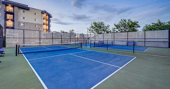 A tennis court is surrounded by a fence and a building.