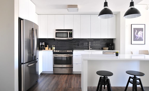 A modern kitchen with a refrigerator, microwave, oven, and bar stools.