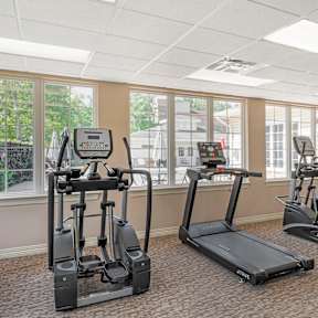 A man and a woman are working out on exercise bikes in a gym.